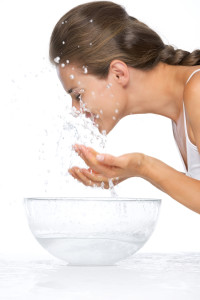 Profile portrait of young woman washing face in glass bowl with water